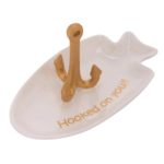 Hooked on You Ring Holder. White ceramic fish-shaped ring holder with gold-colored fishhook to hold rings. Message "Hooked on You" written in gold block letters on inside of dish. Displayed on white background.