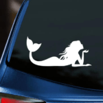 Mermaid Vinyl Decal white decal mermaid laying on stomach blowing kiss displayed on back window of blue car with dark tinting.