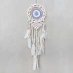 Pastel Small Macrame Dreamcatcher displayed hanging against a light gray backdrop. Hoop on dreamcacher is a white circle. Macrame pattern is a combination of pastel pinks and blues in nesting circles. Tassels are finished with white goose feathers.